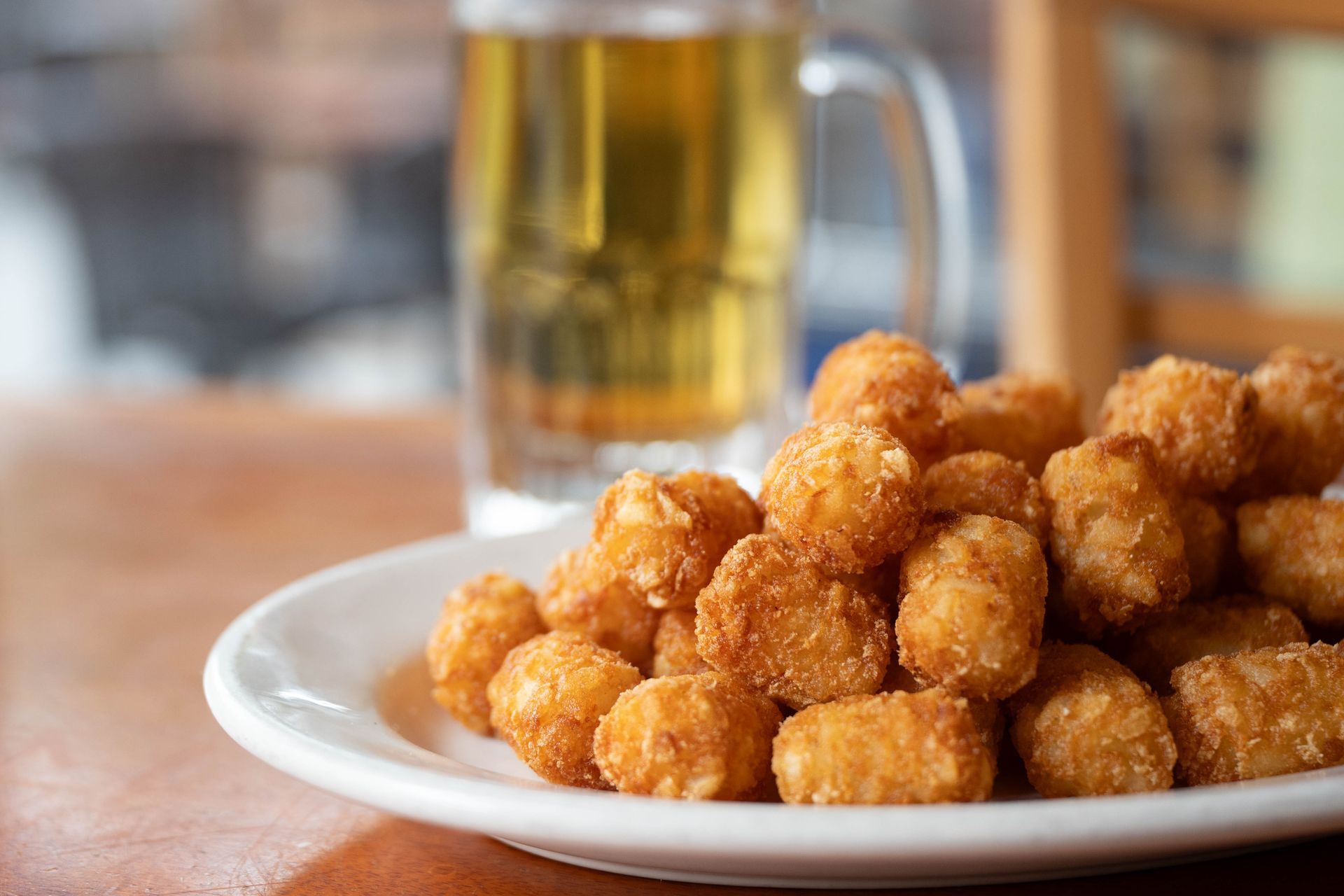 Plate of golden fried dough balls beside a glass of beer on a table