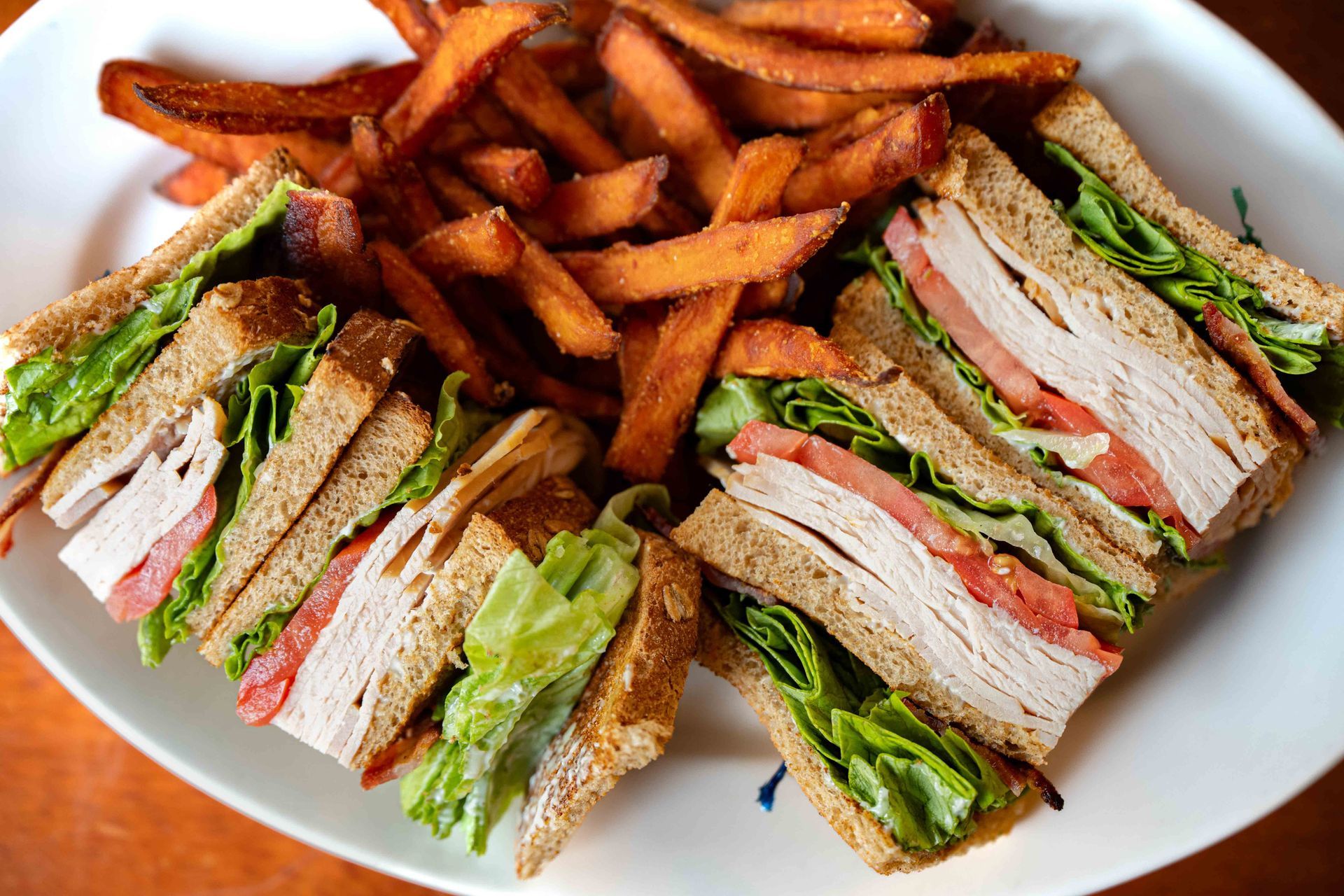 Turkey club sandwich and sweet potato fries on a white plate