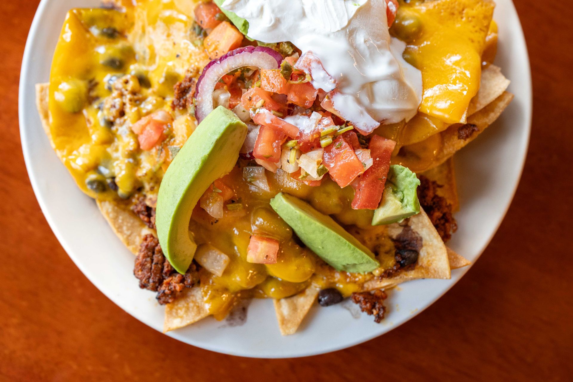 Plate of loaded nachos with melted cheese, salsa, avocado, and sour cream on a wooden table