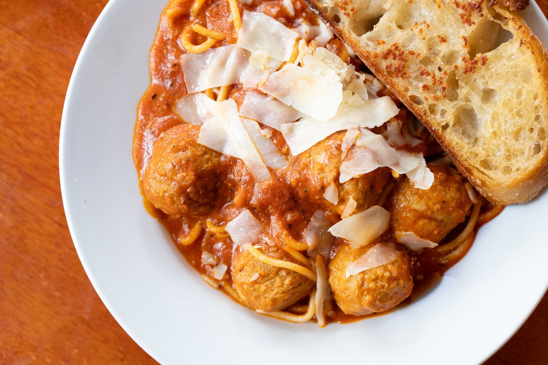 Plate of pasta in red sauce topped with shaved cheese, beside a slice of bread on a white dish