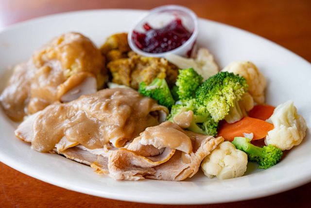 Roast chicken with steamed broccoli, cauliflower, carrots, and cranberry sauce on a white plate
