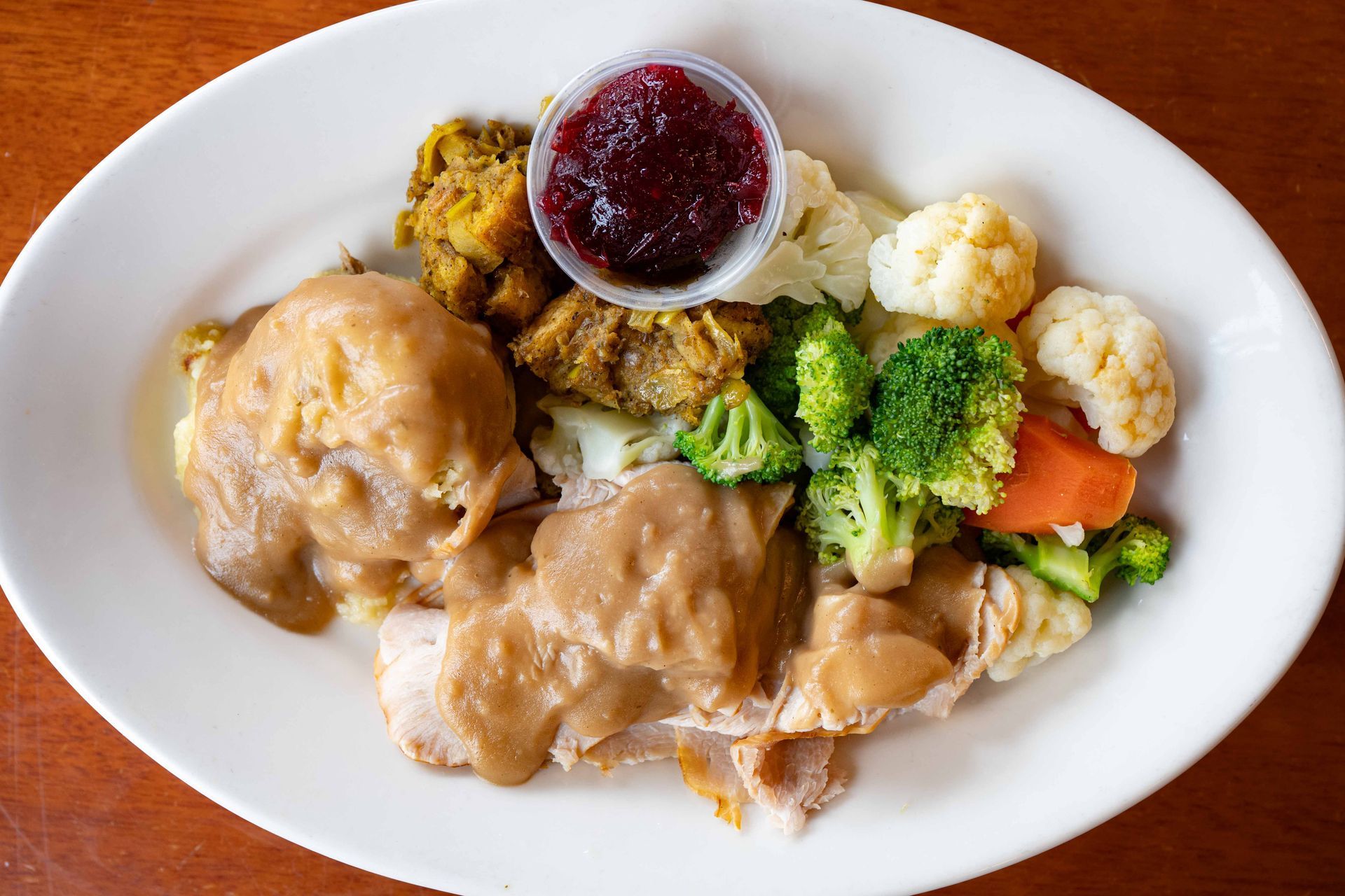 Plate of roast chicken, mashed potatoes, broccoli, cauliflower, carrots, and cranberry sauce
