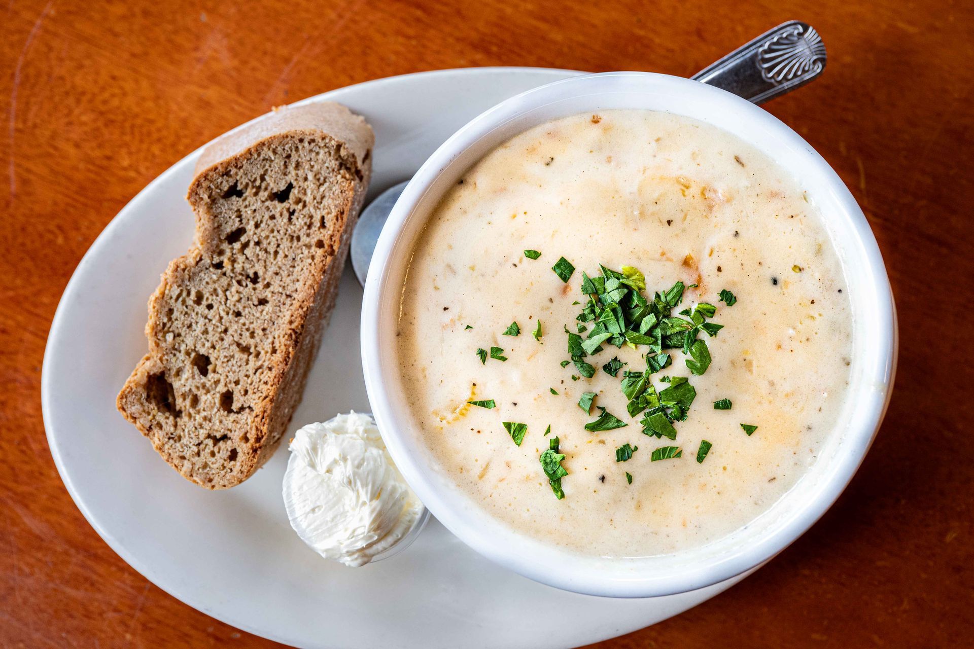 Bowl of creamy soup with herbs, bread slices, and a dollop of cream on a white plate