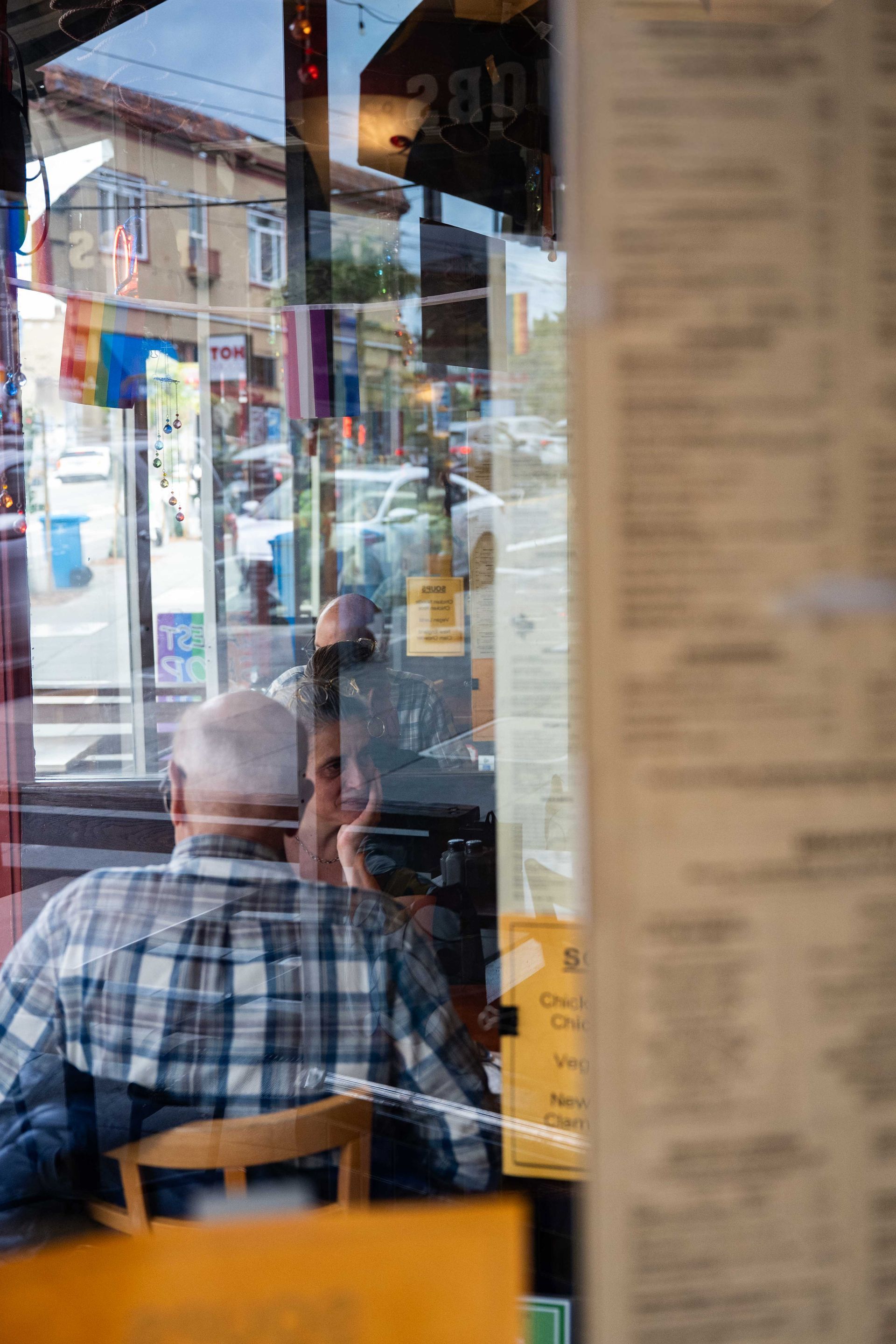 Person seated inside a café, looking out through a window onto a street scene.