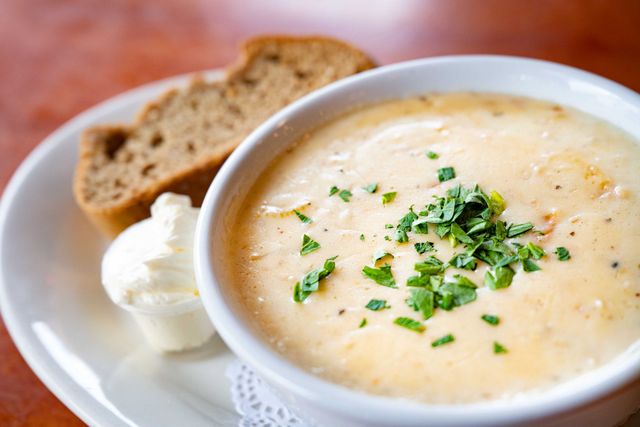 Creamy soup in a white bowl, topped with herbs, beside bread slices on a plate