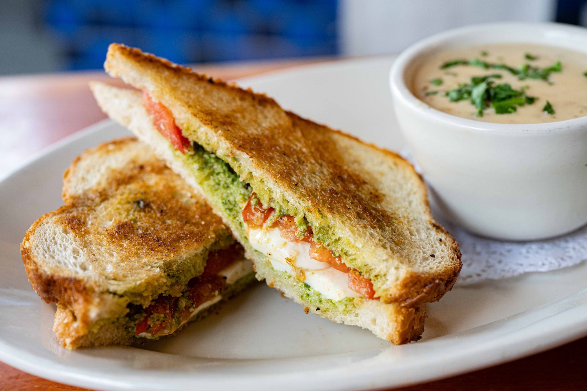 Grilled sandwich halves on a white plate with a bowl of creamy soup on the side