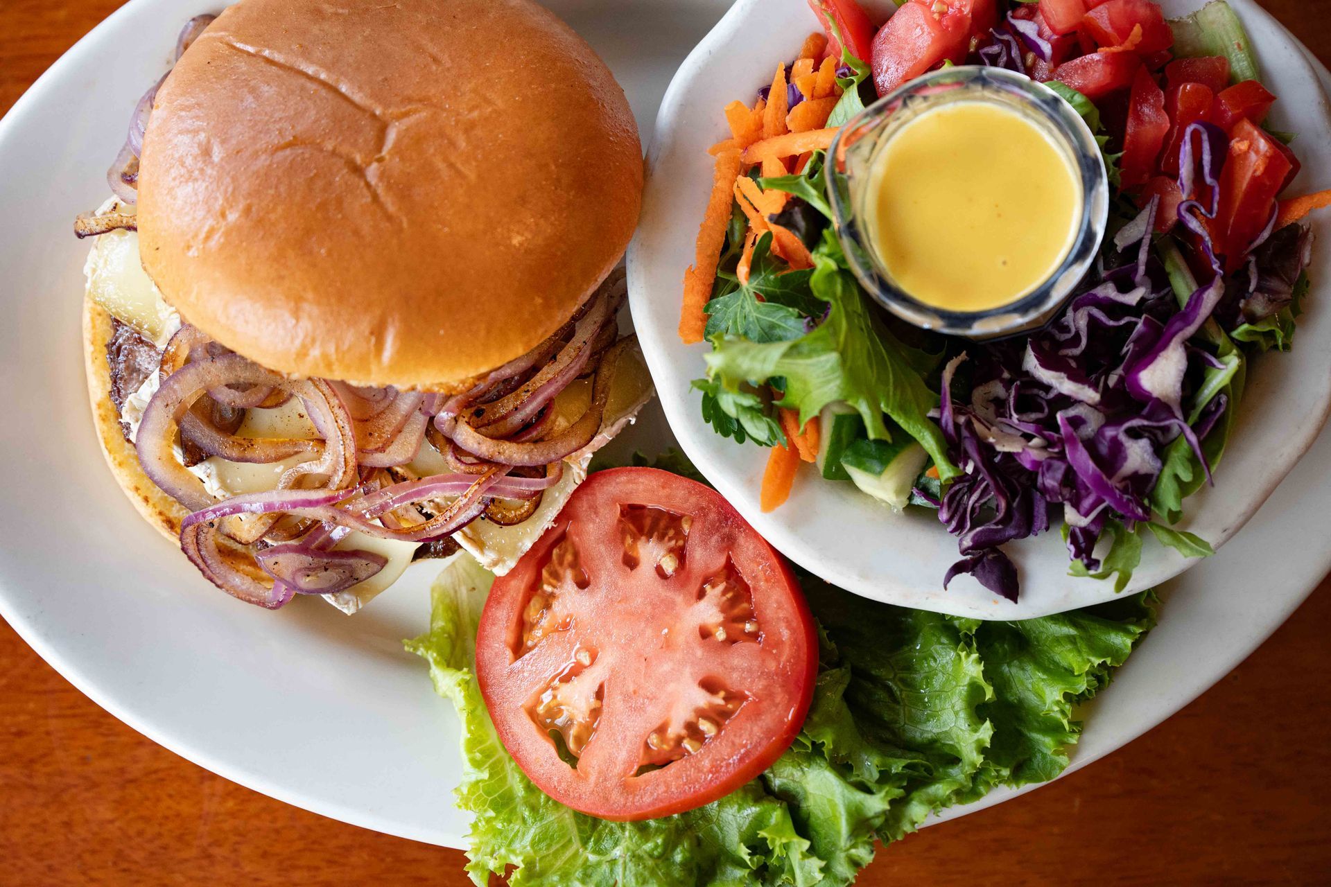 Burger with onion strings and a side salad topped with dressing, garnished with tomato and lettuce.