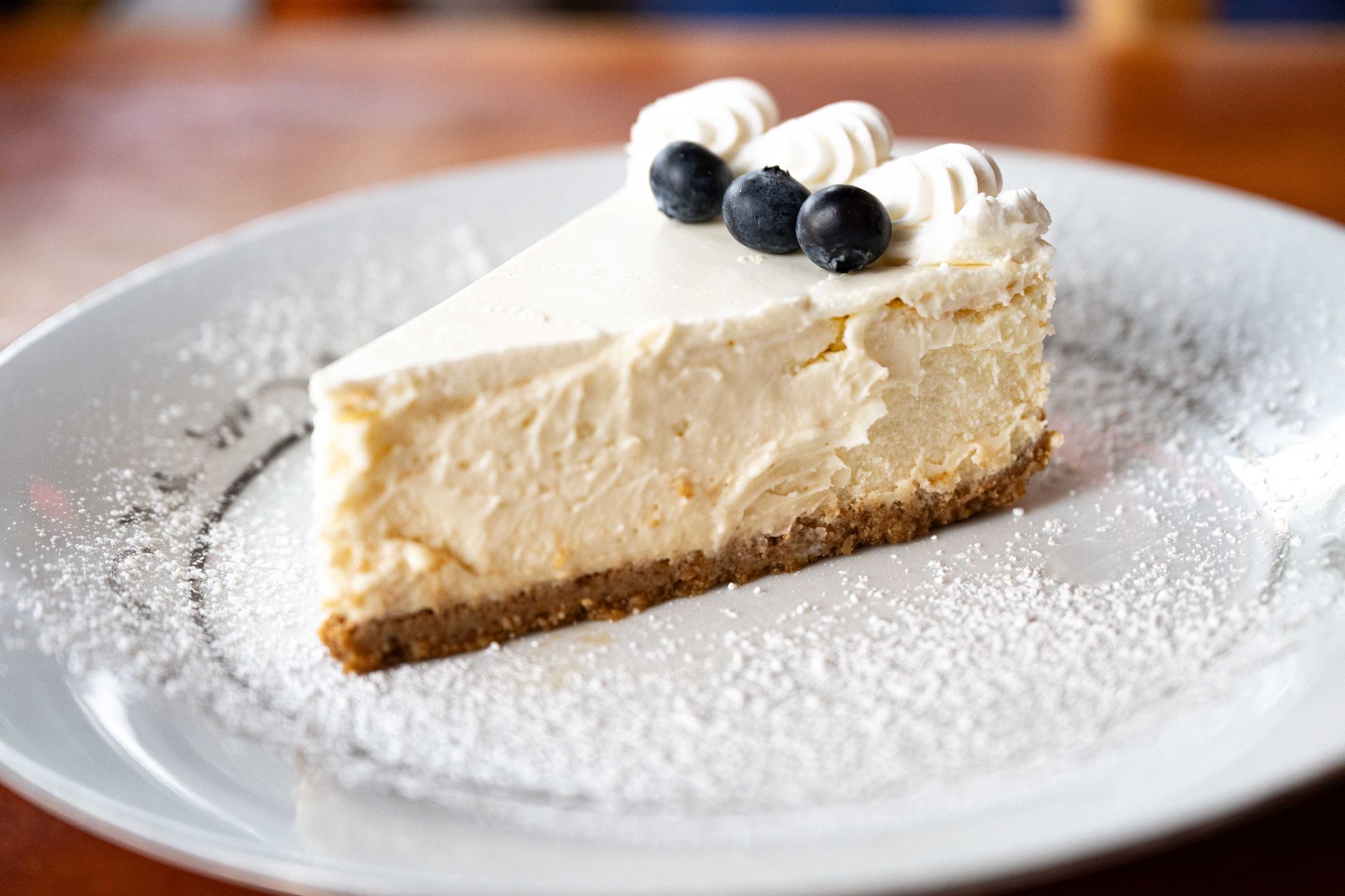 Slice of creamy cheesecake topped with whipped cream and blueberries on a white plate