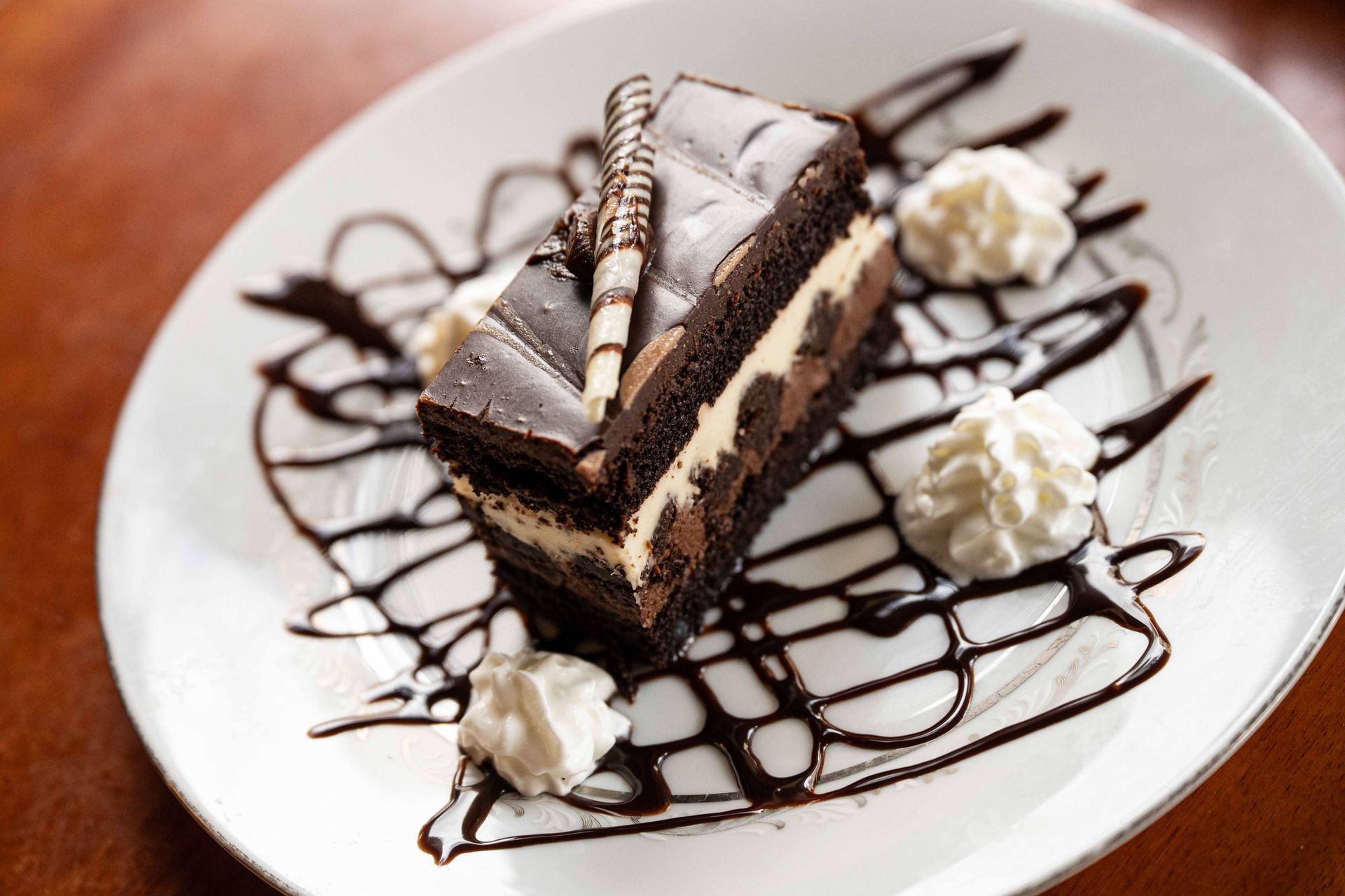 Chocolate cake slice with whipped cream and chocolate drizzle on a white plate