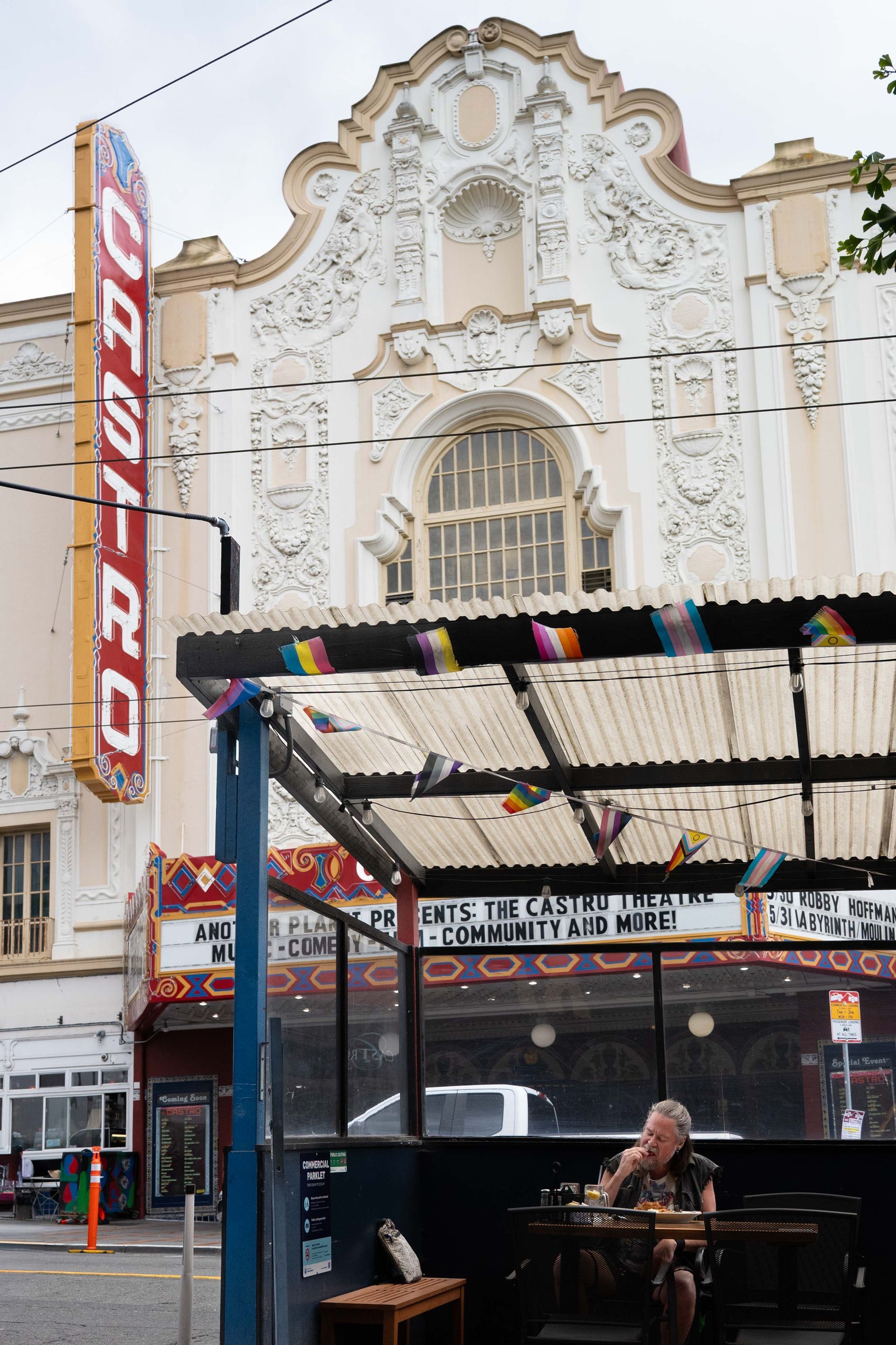 Ornate theater facade above a street-level patio with a seated person and red vertical theater sign