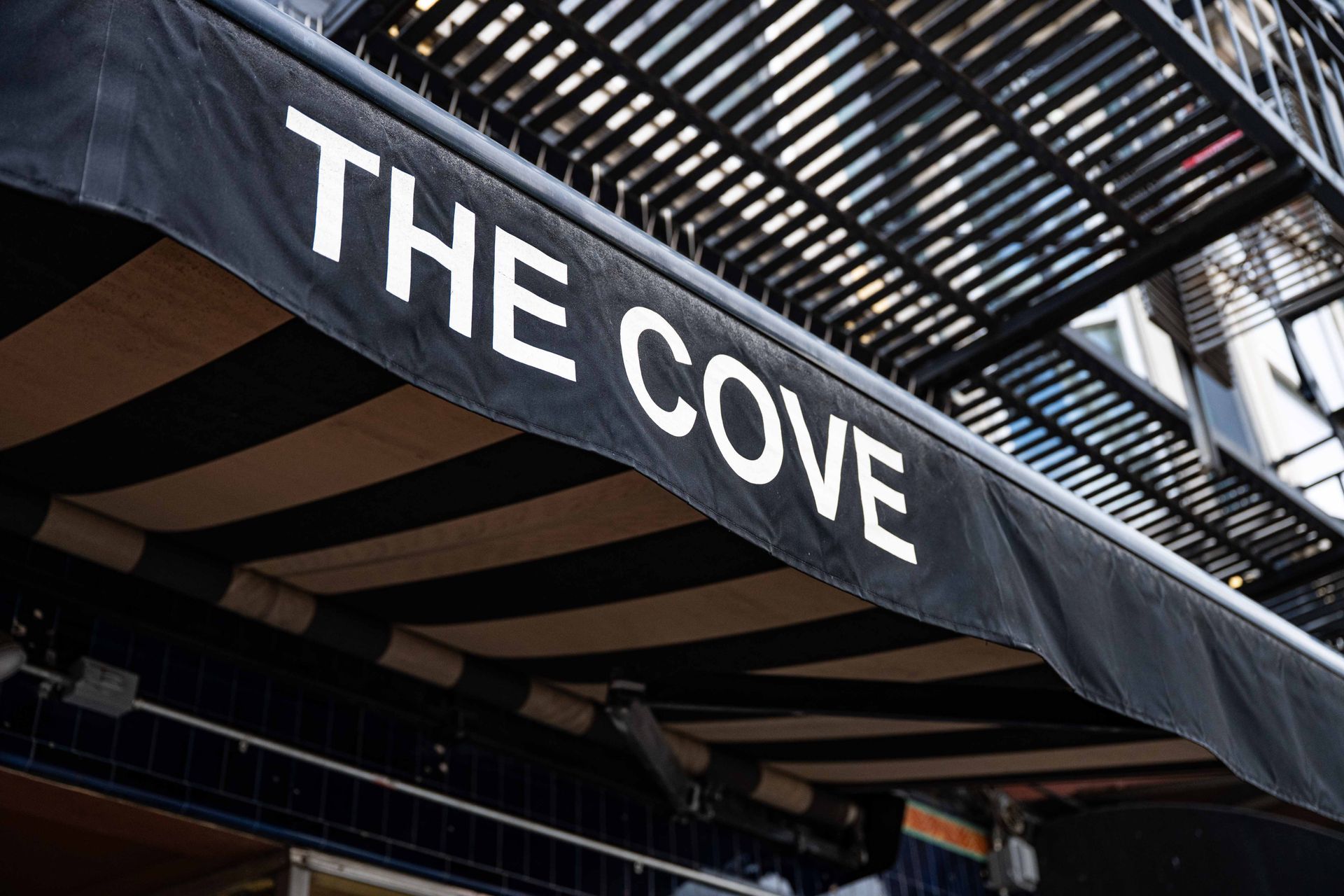 Black awning with white “THE COVE” lettering beneath a striped canopy