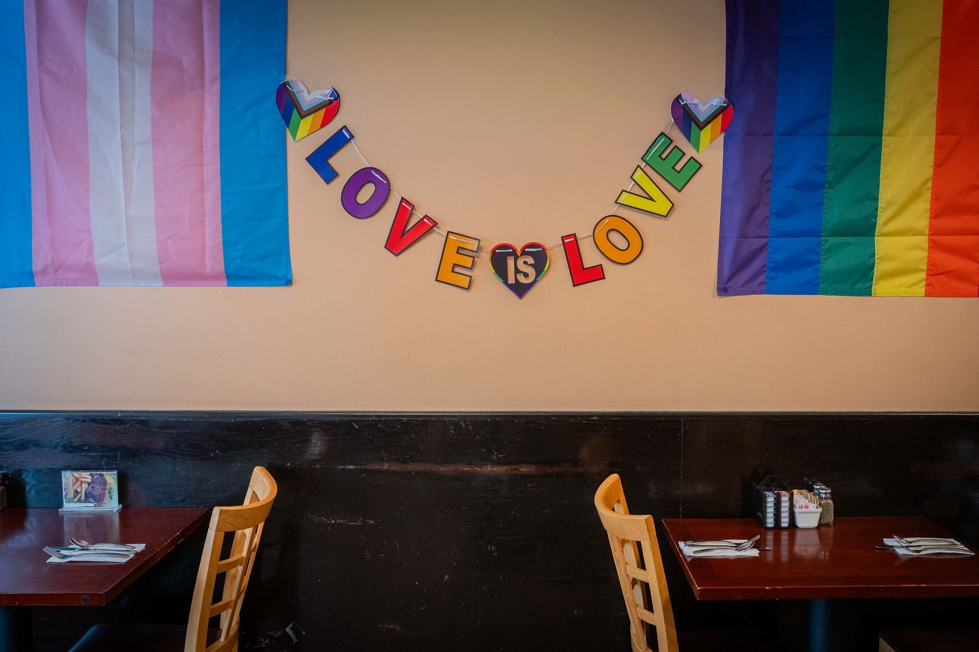 Colorful “LOVE IS LOVE” banner on a wall above empty restaurant booths