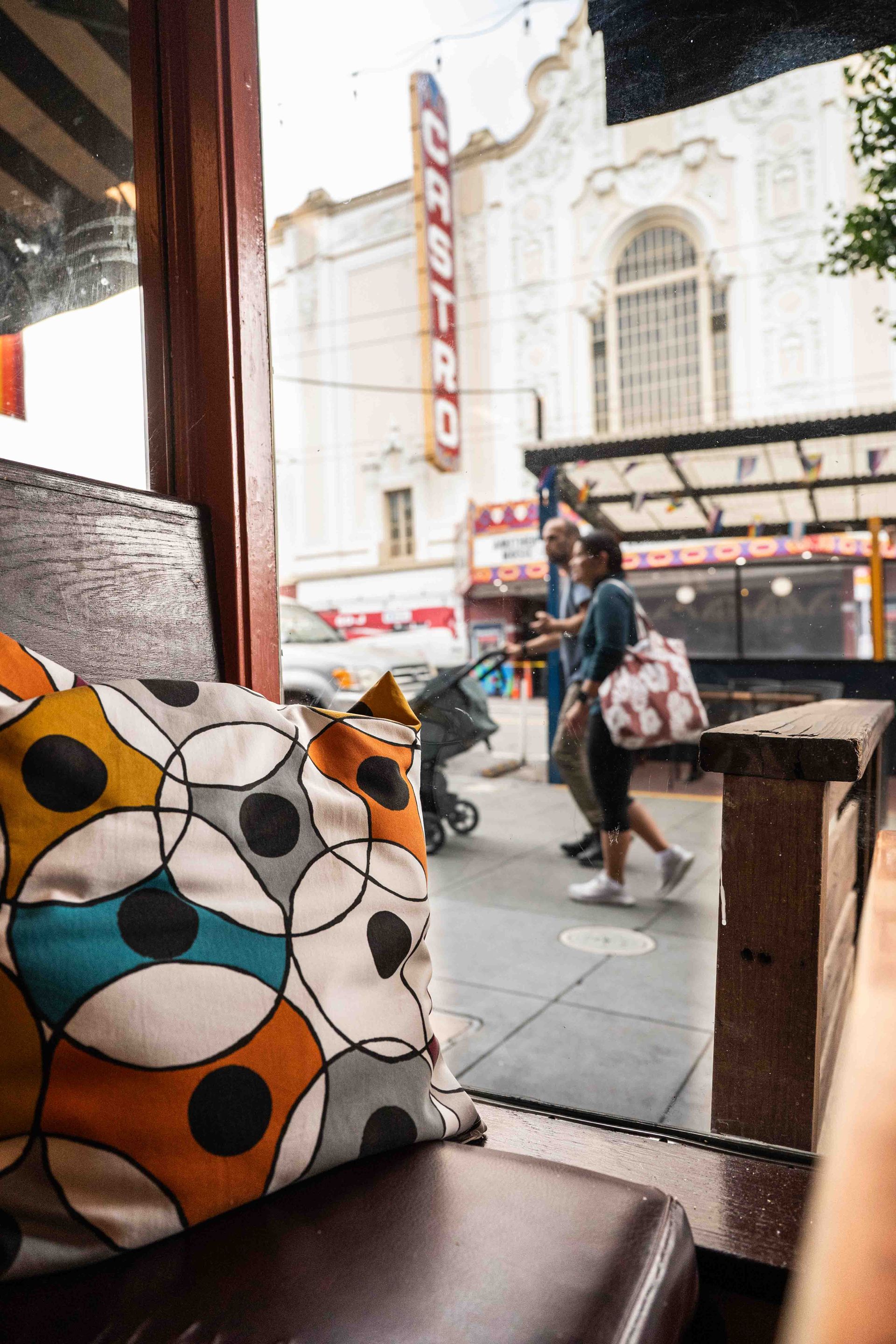 Café window view of a person walking past a street with a theater marquee; colorful patterned cushion in foreground