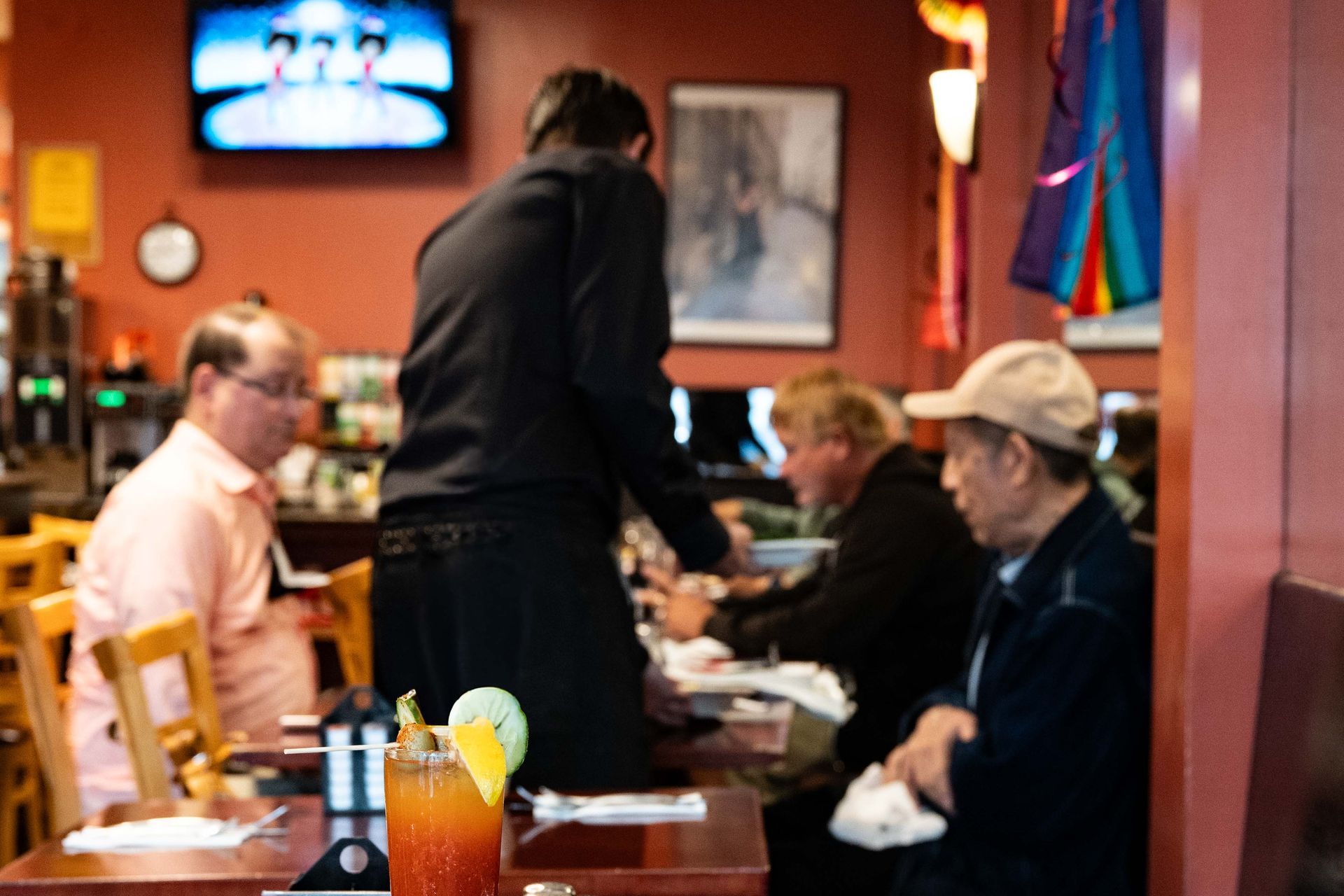People seated at a restaurant table with drinks, while a server stands nearby.