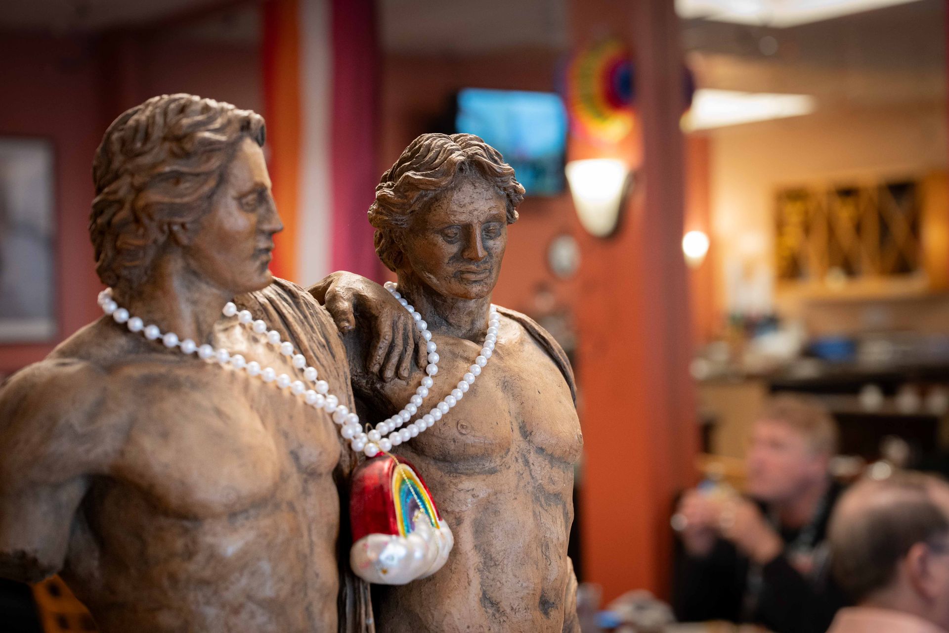 Two small statues with white bead necklaces in a museum display, with a blurred crowd behind them.