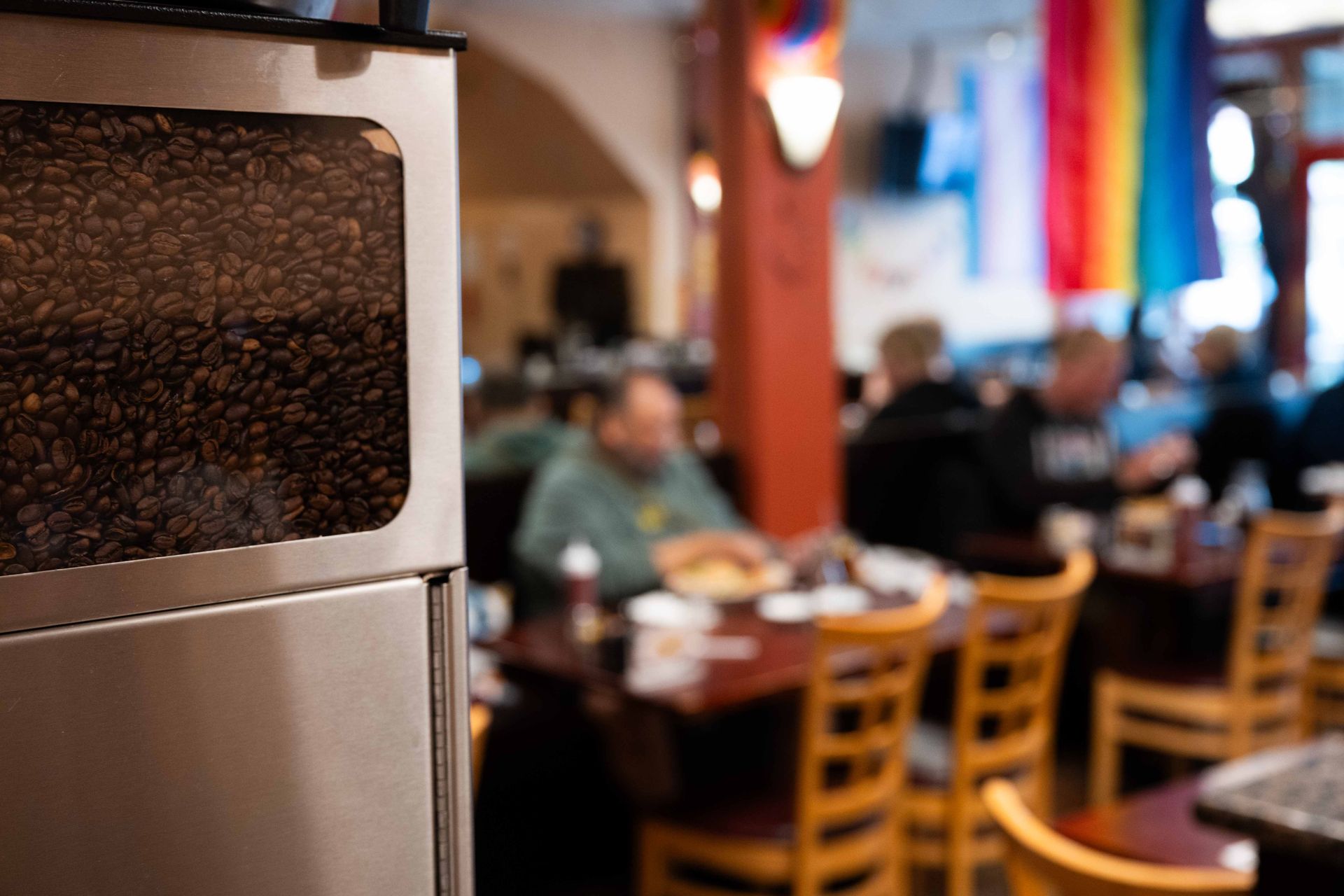 Restaurant interior with wooden chairs and diners, viewed past a coffee machine in the foreground