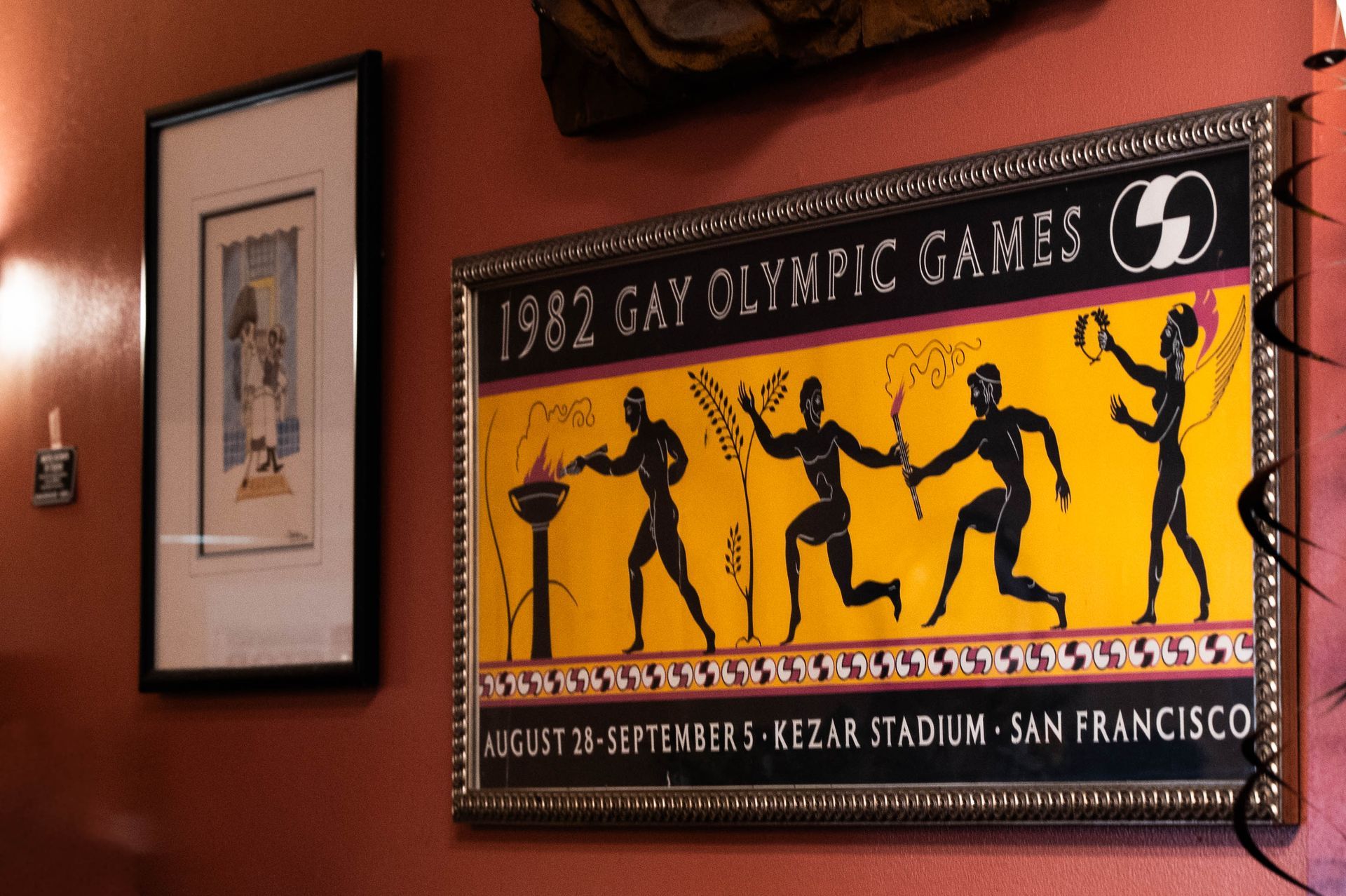 Framed 1982 Gay Olympic Games poster in yellow and black on a red wall