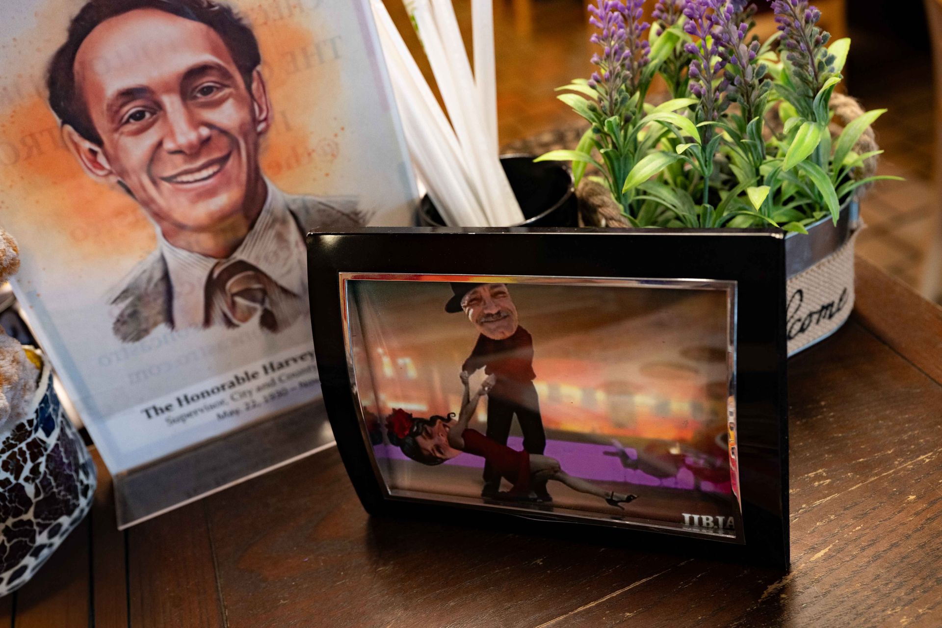 Memorial display with framed portrait, small screen showing a dancer, and flowers on a wooden table