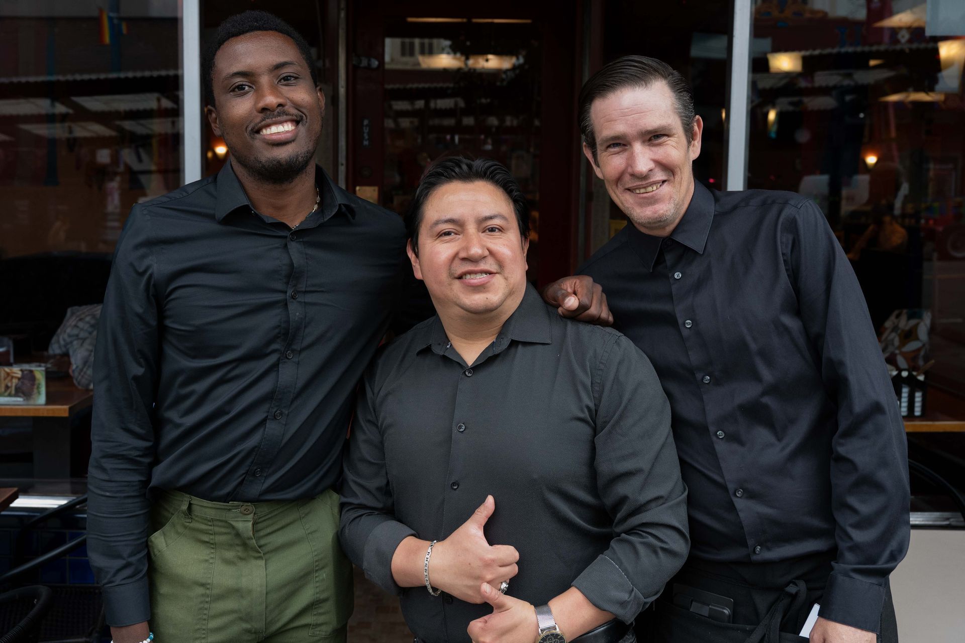 Three smiling people posing together outside a restaurant.