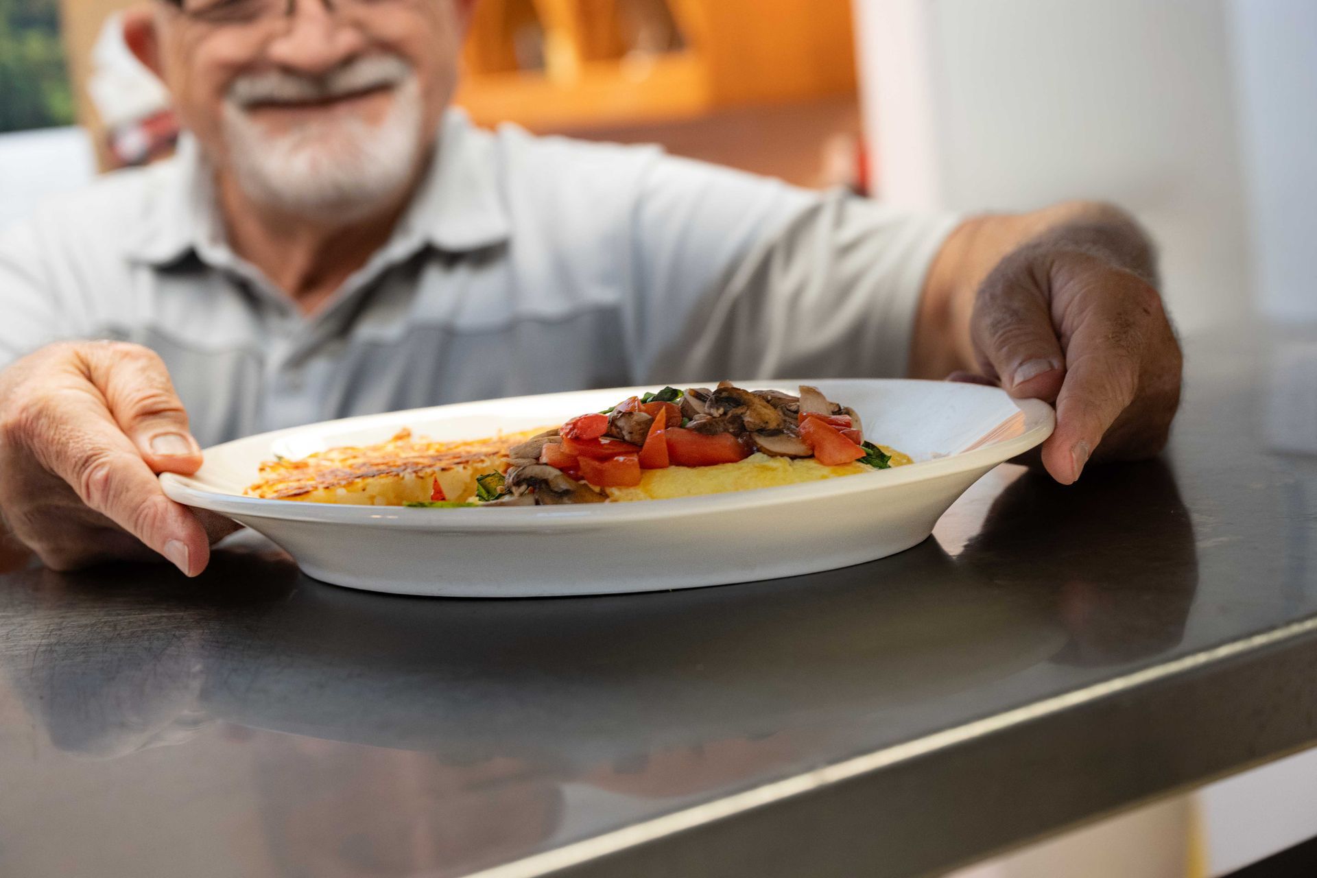 Person holding a plate of food toward a table, with a meal of vegetables and pasta in the foreground