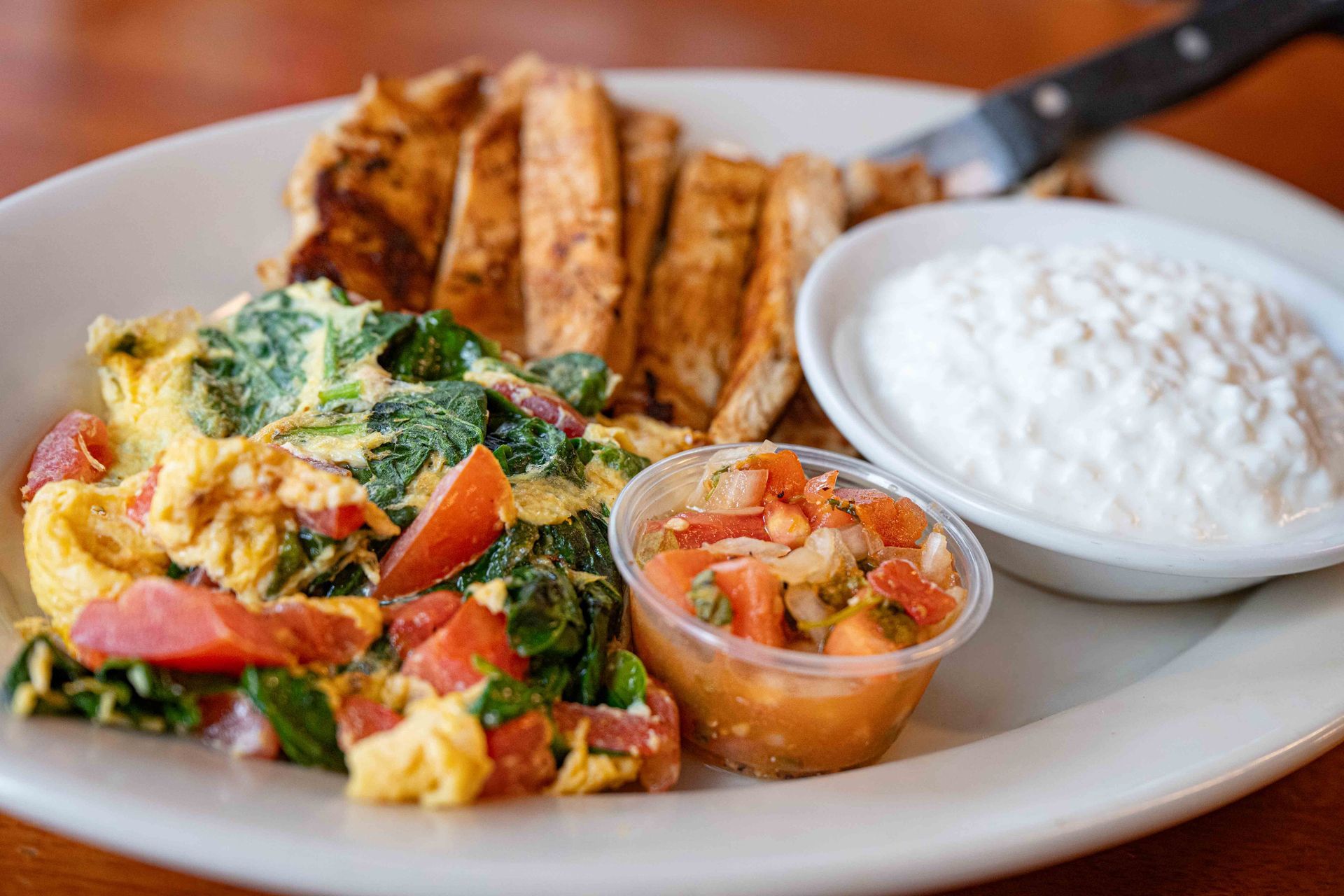 Scrambled eggs with vegetables, toast, salsa, and a bowl of sour cream on a plate