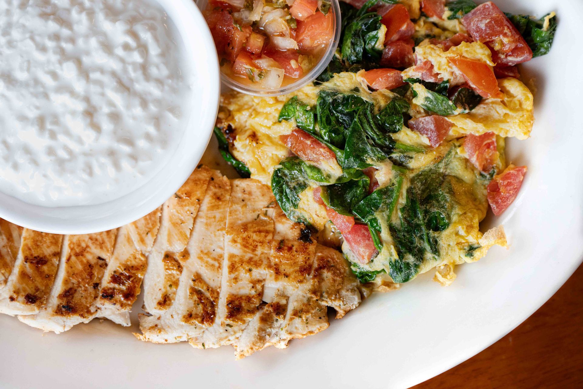 Plated grilled chicken with colorful vegetables and a side of white sauce