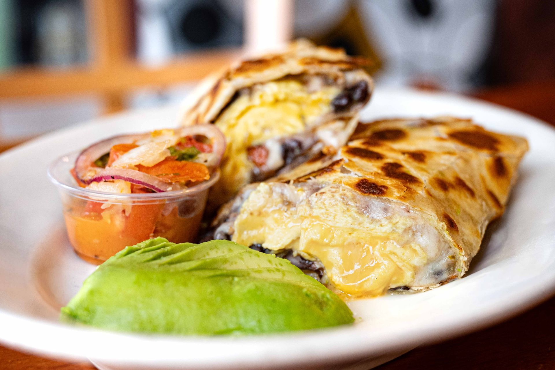 Two grilled burritos on a plate with guacamole and salsa