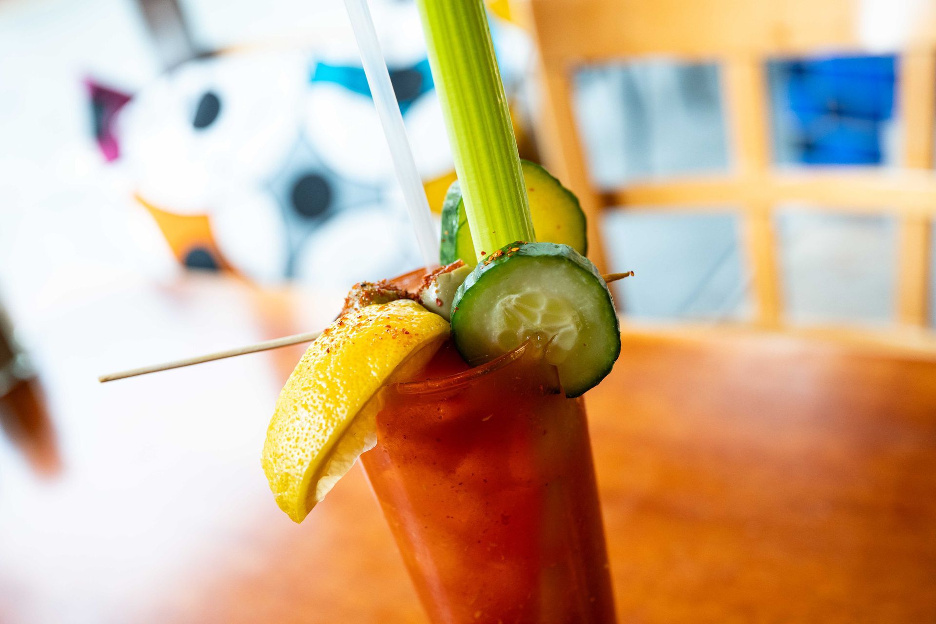 Bloody Mary cocktail with celery, cucumber, lemon, and a toothpick garnish on a wooden table