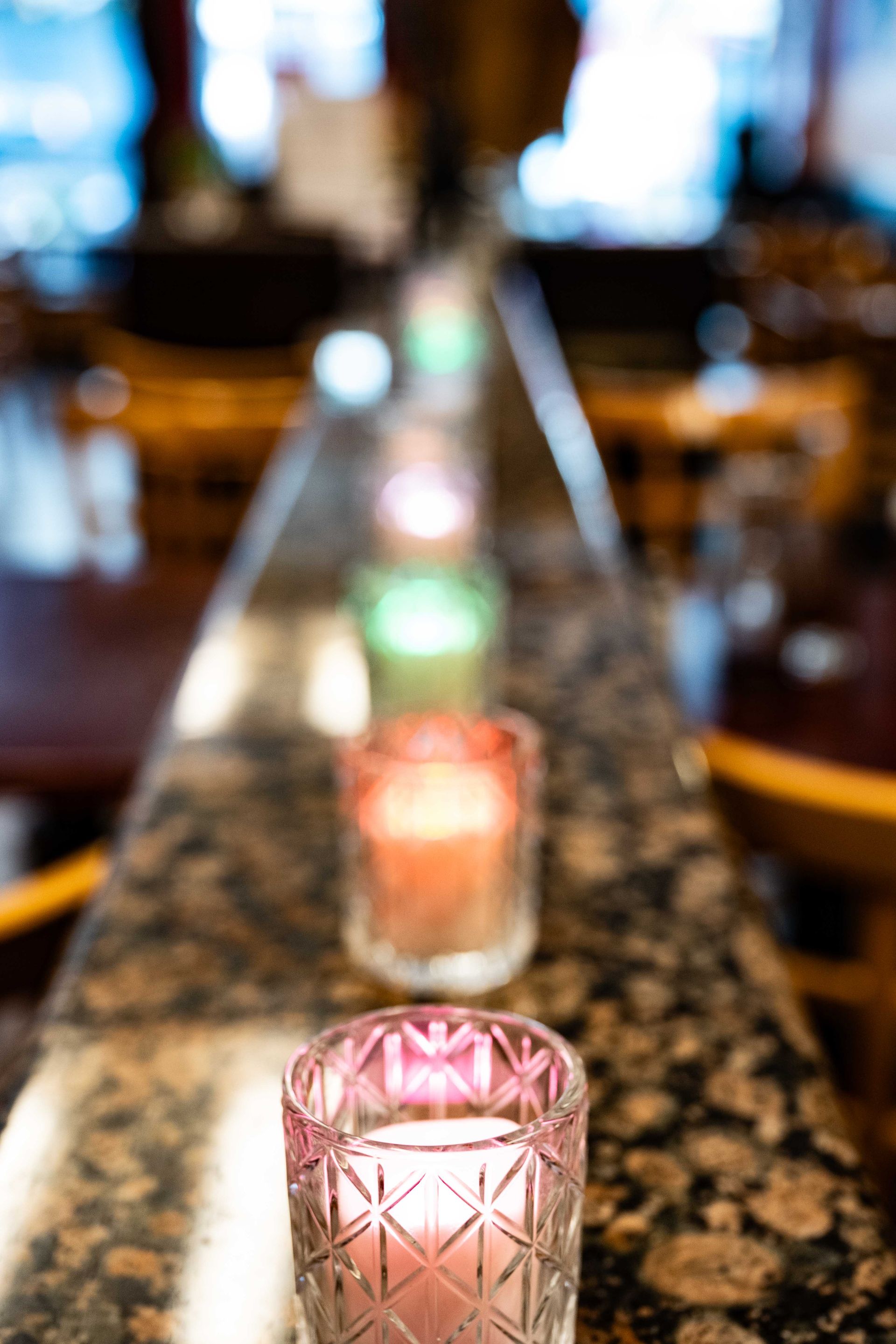 Row of pink votive candles glowing along a granite bar in a dim restaurant