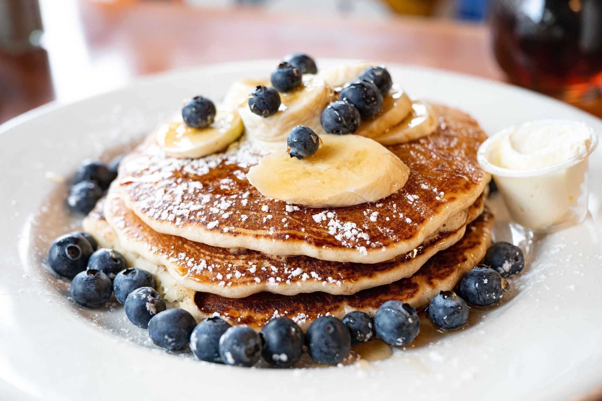 Stack of pancakes topped with blueberries and banana slices, served with whipped cream on a white plate