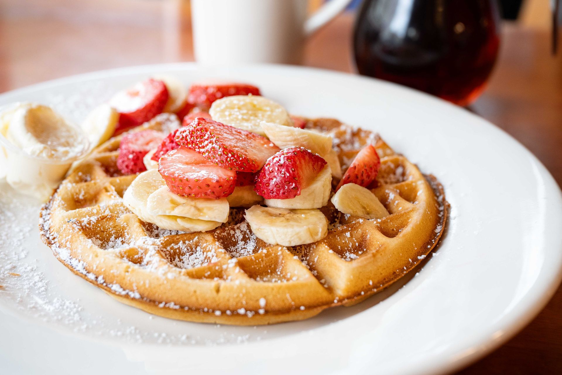 Powdered waffle topped with strawberries and banana slices on a white plate