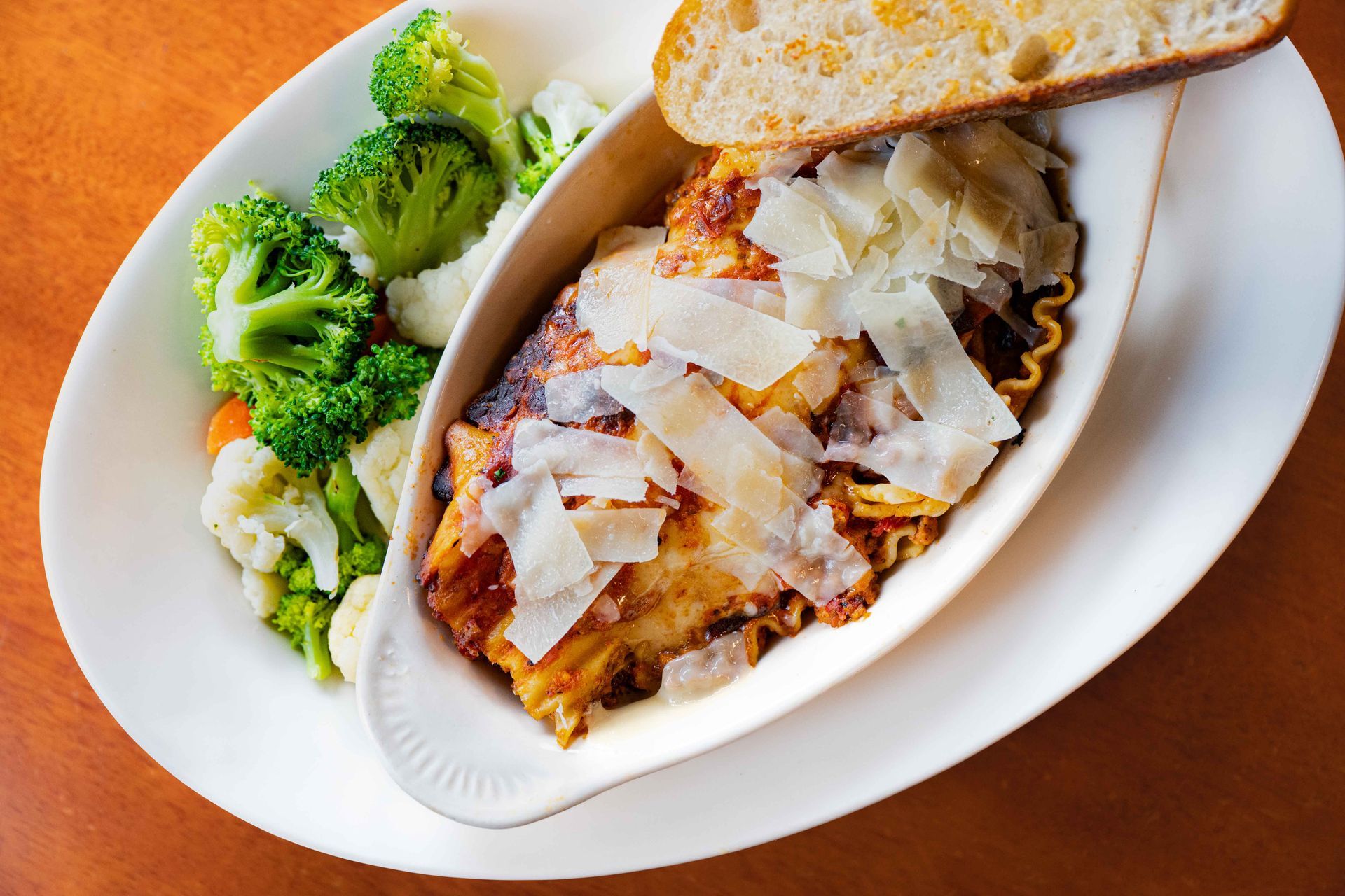 Baked chicken parmesan with broccoli on a white plate and toasted bread on a wooden table