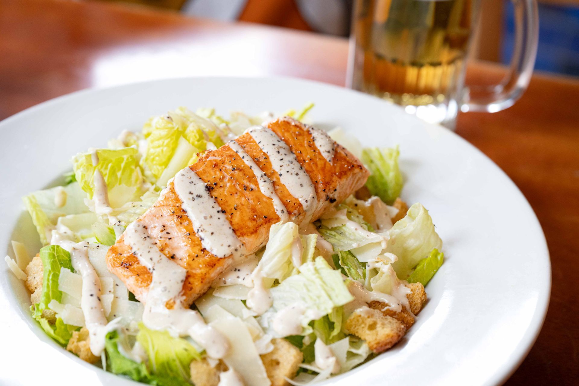 Grilled chicken Caesar salad in a white bowl on a table with a glass of iced tea