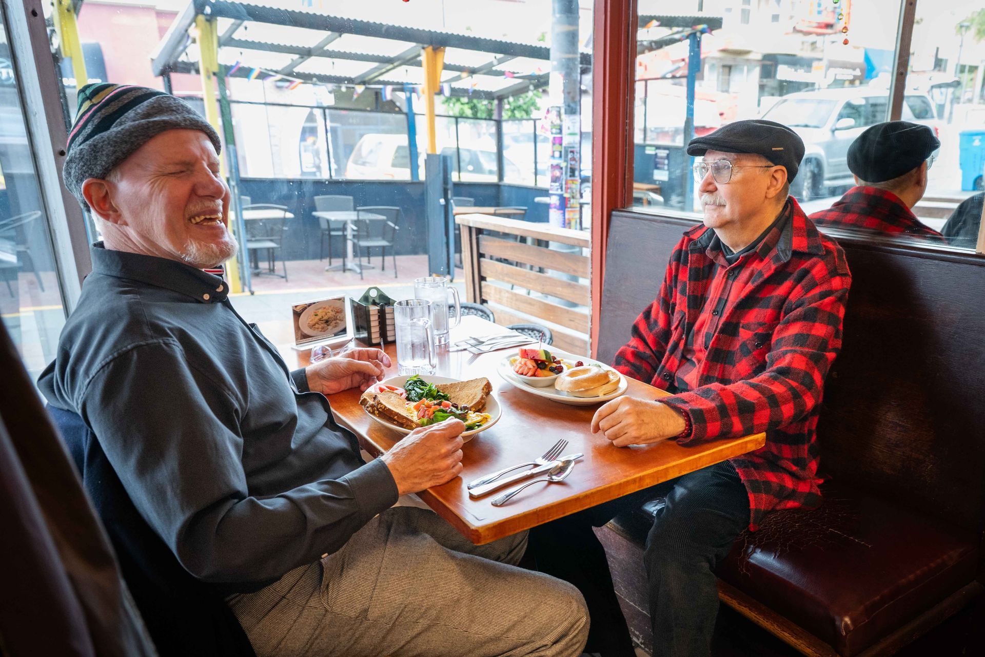 Two men in casual clothes chatting over lunch at a café window table