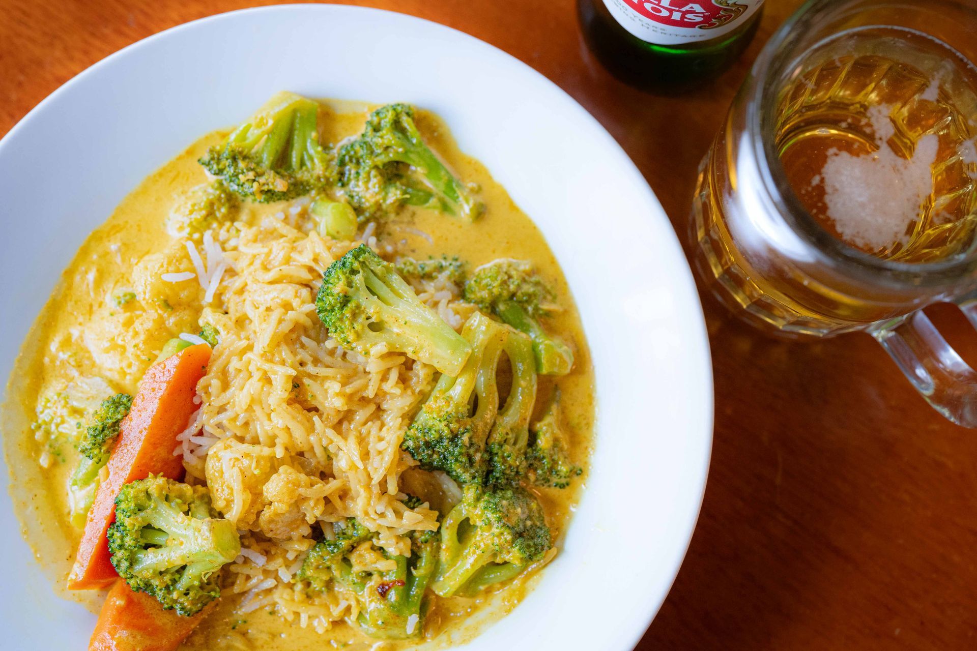 Plate of creamy broccoli rice with a sausage on a wooden table beside a glass mug