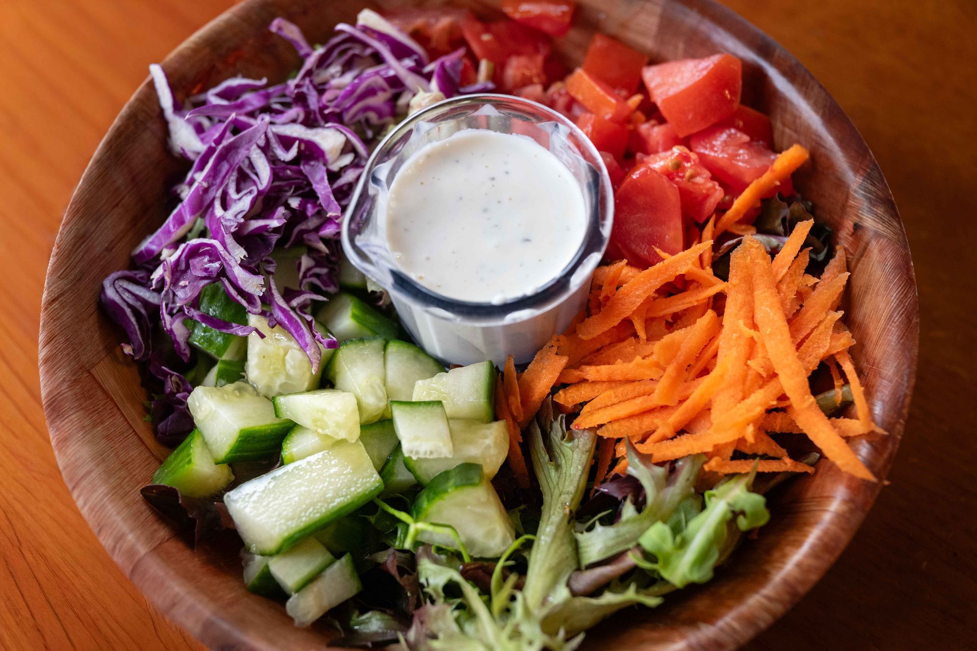 Colorful salad bowl with shredded purple cabbage, cucumbers, carrots, peppers, greens, and a creamy dressing cup.