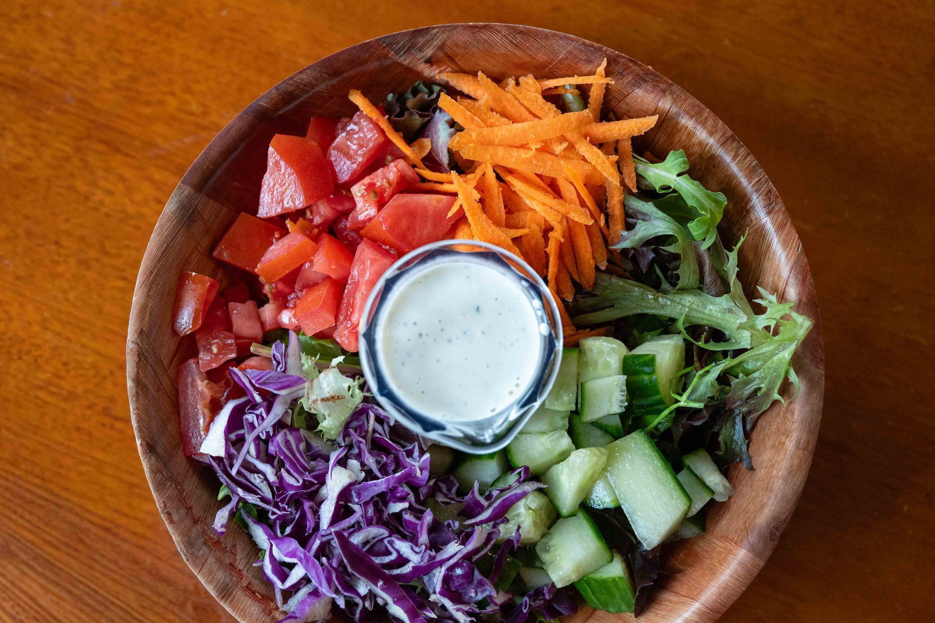 Colorful salad bowl with vegetables arranged around a central dipping sauce on a wooden table