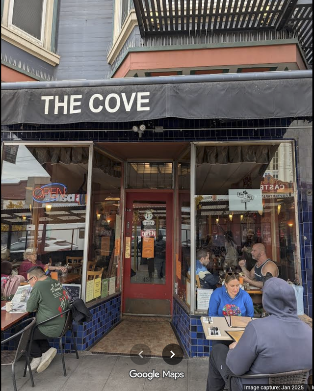Storefront of The Cove café with outdoor seating and customers dining under a black awning.