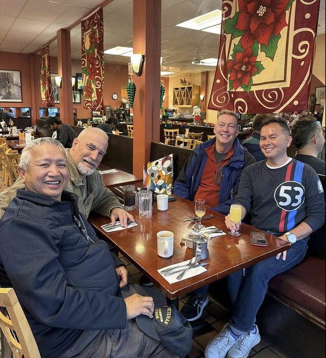 Friends smiling at a restaurant table, with drinks and red floral wall hangings in the background