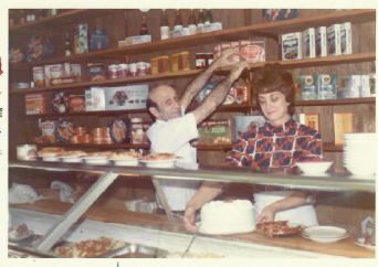 Bakery counter with two workers arranging bread and pastries on shelves and display cases.