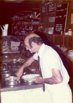 Chef washing dishes at a restaurant sink, with pots and plates on the counter.
