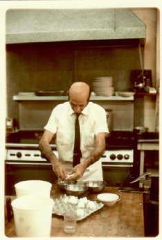Chef kneads dough at a kitchen counter with bowls and utensils nearby.