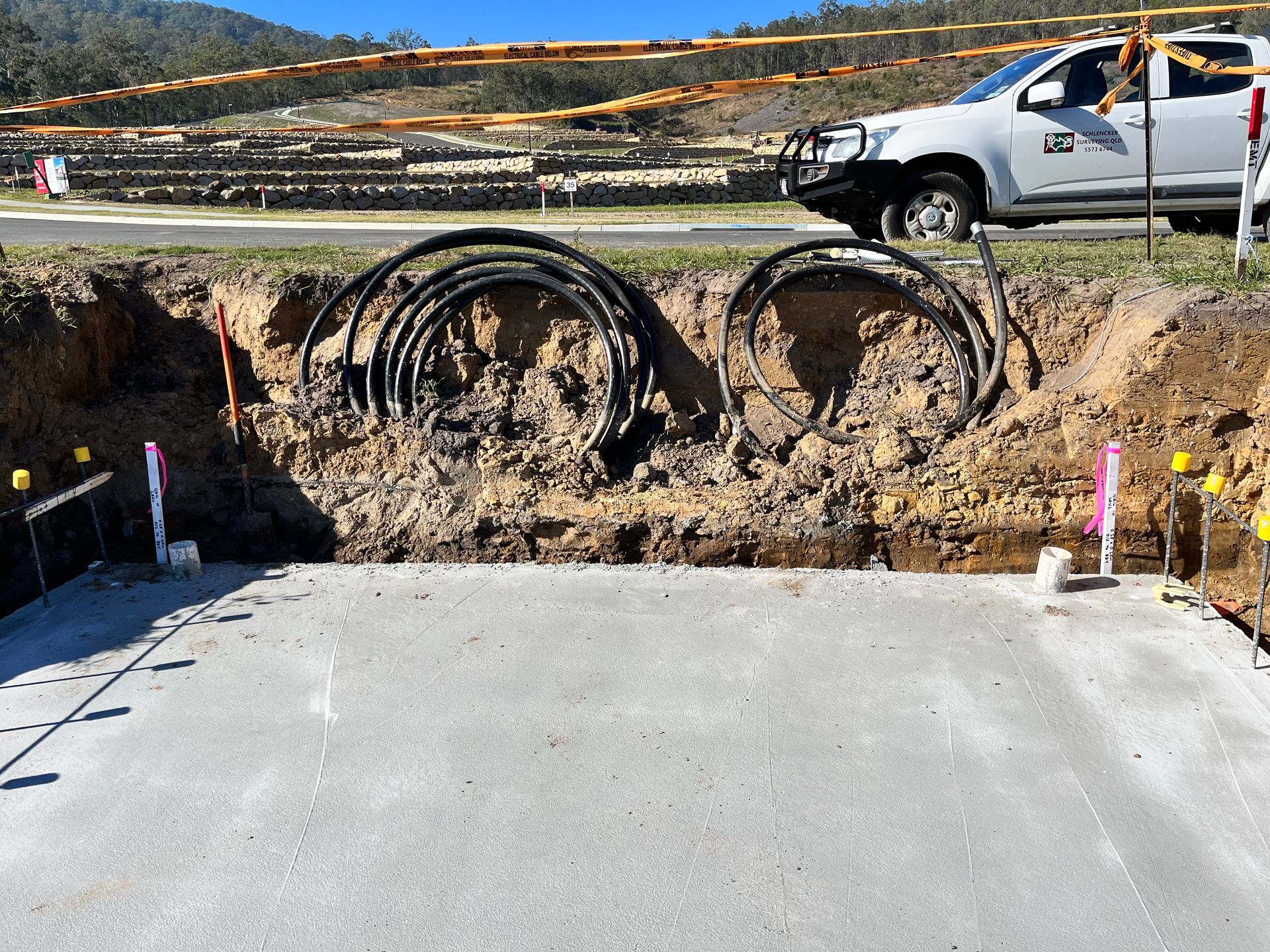 A white truck is parked next to a pile of pipes in the dirt.