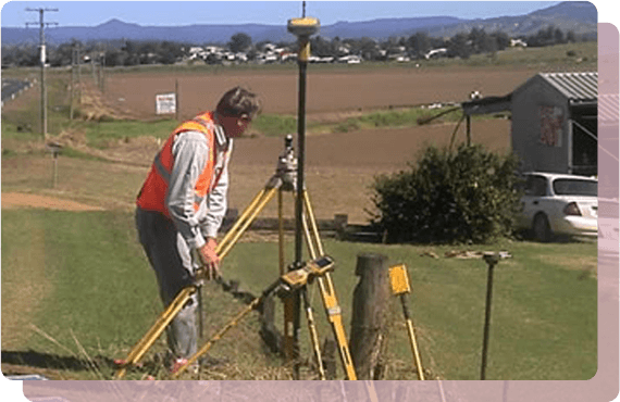 A man in an orange vest is working on a tripod in a field.