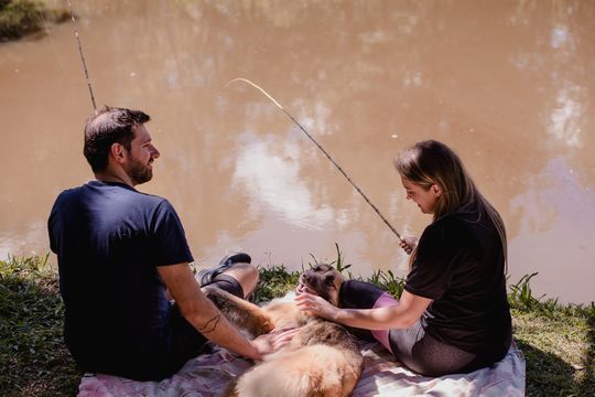 Um homem e uma mulher estão sentados em um cobertor com um cachorro e pescando em um lago.