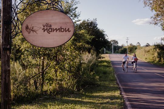 Duas pessoas andam de bicicleta por uma estrada próxima a uma placa que diz vila bambu.