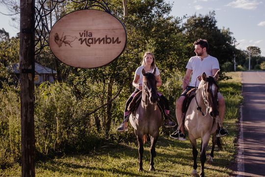 Um homem e uma mulher estão andando a cavalo em frente a uma placa que diz villa mambo