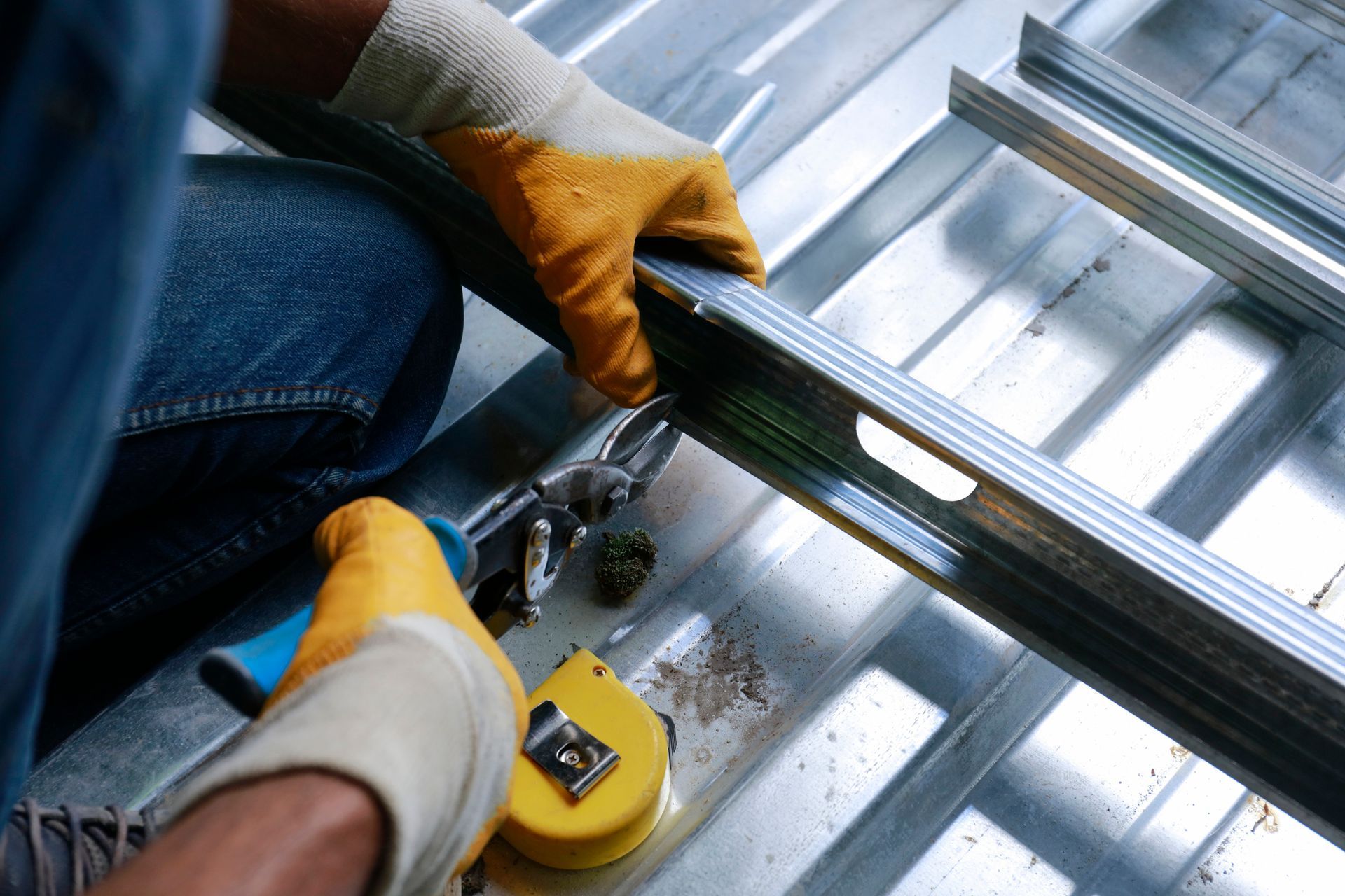 Person wearing work gloves cutting metal stud with pliers on a metal surface.