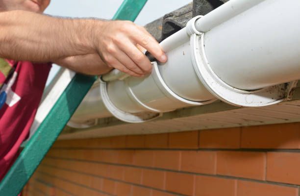 Person installing white guttering on a brick building using brackets.