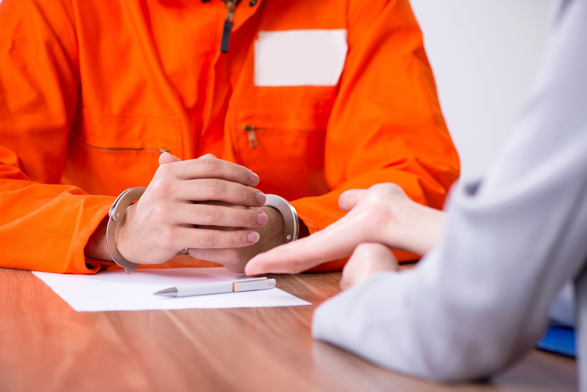 Person in orange prison uniform with handcuffs, meeting with a person pointing at a document on a table.